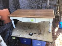 Photo of rectangular coffee table with wooden top and white painted legs, showing a drawer and some usage marks on the surface.