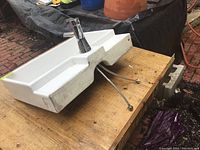 White ceramic or porcelain rectangular countertop sink placed on wooden surface shown from side angle, showing faucet and attached water supply lines.