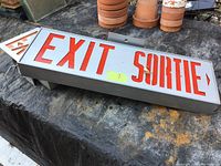 Large rectangular bilingual exit sign showing 'EXIT' and 'SORTIE' with arrow, placed on surface with some wear.