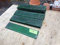 24 green textured glass tiles in stacks on a wooden surface with terracotta pots in background
