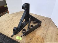Two handmade black iron wall brackets with decorative scrollwork positioned on a wooden surface photographed from an angle to show design and structure.