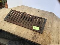 Cast iron floor vent register photographed on a wooden surface with visible rust and wear.