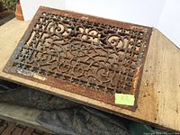 Cast iron floor register with detailed scrollwork pattern and visible rust on surface.
