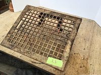 Iron floor register laid flat on wooden surface showing grid design and frame