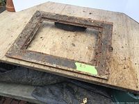 Top-down photo of a rectangular iron frame with rust and wear placed on a wooden surface.