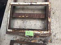 Rectangular iron frame with rust and chipped paint, showing wear and signs of age on a concrete surface.