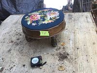 Top view of the round needlepoint footstool showing the floral design on the navy cushion and the wooden legs.