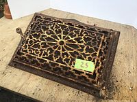 Photo of antique cast iron wall register vent showing ornate openwork grille and side adjustment lever.