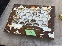 Metal wall register vent cover with decorative arch pattern and visible rust and paint chipping.