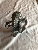 Black Alien figure on a light fabric surface, showing front and top side with detailed head and clawed hands.