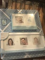 Two baby photo frames and one blue poster board on wooden chair. Frames are new in package, poster board lightly used.