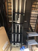 Photo showing the black and silver metal frame ladder of the loft bunk bed leaning against wall with parts assembled or stacked nearby.