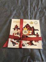 Front view of the packaging showing the presentation folder with colorful Canadian illustrations and the silver coin in the center wrapped with a red ribbon