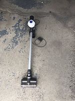 Dyson V6 Slim cordless vacuum cleaner lying on a concrete floor, visible tubular handle and cleaning head.