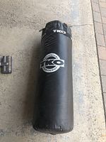 Full view of black TKO branded heavy bag placed horizontally on ground showing logo and weight indication.