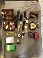 Overall lot with watches, tool kit, compass, and accessories spread on fabric