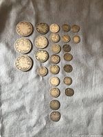 Top view of entire coin collection showing all 23 coins laid out on fabric background, arranged by size and denomination.
