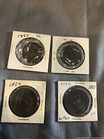 Four pre-Canada copper coins from 1857, each encased in cardboard holders with plastic windows. The coins show the Bank of Upper Canada inscription with distinct aged patina and details.