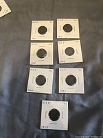 Seven US Indian Head pennies in white paper holders with handwritten dates and face values.