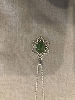 Close-up of the flower-shaped sterling silver pendant with central green stone showing elegant openwork design.