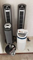 Three Lasko tower fans and one Homedics air purifier arranged in a corner showing front and side views.