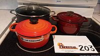 Orange Le Creuset and red Martha Stewart Dutch ovens front view, on stove