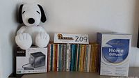 Overview of lot with Snoopy plush, Sony clock radio box, vintage Peanuts books, and Home Diffuser box