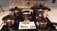 All pieces arranged on stovetop showing stockpot, large saucepan with lid, saucepans and double boiler insert