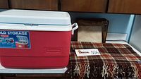 Photo showing Coleman red and white 48 qt ice chest next to folded Pendleton stadium blanket and original zipper case with pillow.