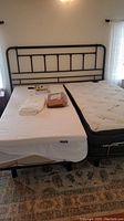 Full view of two adjustable twin bases with mattresses against black metal headboard