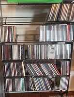 Five shelves of assorted music CDs on metal shelving unit