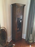 Full front view of the oak grandfather clock showing its height, shape, and placement in a room corner.