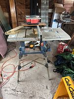 Front view of Ryobi 10 inch table saw on stand showing the table surface, adjustment knob, and saw blade guard.