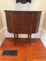 Front view of the wood side table showing three drawers and compartments on the sides, standing on turned legs.