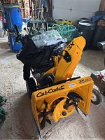 Full view of yellow Cub Cadet snowblower with attached black Atlas snow cab and manual resting on top