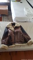 Coat laid open on bed showing front view, brown leather exterior with shearling trim
