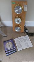 Full setup showing oak mounting board with three brass-cased gauges, two instruction manuals, and power adapter cable.