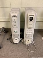 Two beige NOMA oil-filled radiator heaters standing side by side with cords visible, showing analog dial heater on left and digital display heater on right.