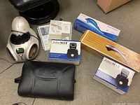 Overview of all items in the lot including Skinfive device, two JointMax vibrating massagers in box, handheld percussion massager box, black lumbar support cushion, and therapy pamphlets.
