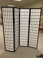 Full view of four-panel folding privacy screen with dark wood frame and white fabric face with grid pattern.