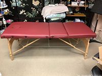 Full view of the three-section maroon portable massage table set up in a room.