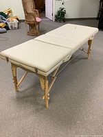 Side angled view showing the cream-colored padded surface on wooden foldable legs and support ropes for stability.