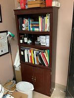 Front view of the dark wooden office bookcase filled with books, binders, and folders on shelves, and cabinet doors closed below.
