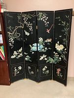 Front view of a four-panel wooden screen with intricate painted floral and bird designs on black background.