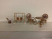 Photo showing a porcelain mortar and pestle, miniature swing set with two seats, and a pair of chairs with a table, all featuring porcelain inserts with painted floral and romantic scenes and ornate gold-tone metal frames.
