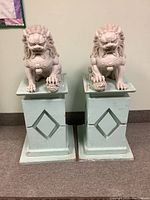 Front view of both white stone guardian lion statues on pale green wooden stands side by side