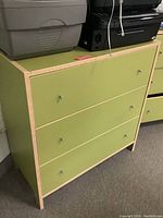 Front angled view of green IKEA 3 drawer dresser with two knobs on each drawer and wood edge trim. Some wear visible on surface.