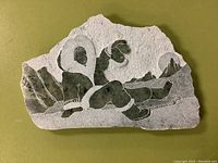 Full view of soap stone carving showing two figures in fur-lined parkas sitting outdoors with mountains in the background.