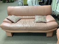 Front view of pink leather loveseat with two floral pillows