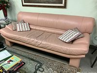 Front-left view of pink leather sofa with three throw pillows on left and one on right, showing seat wear